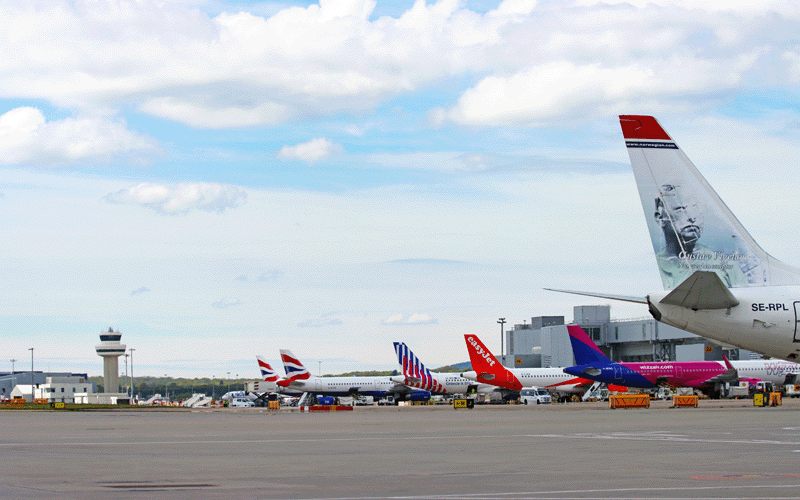 a photo of the airfield at London Gatwick, with multiple planes from various airlines on stand, and the control tower behind them